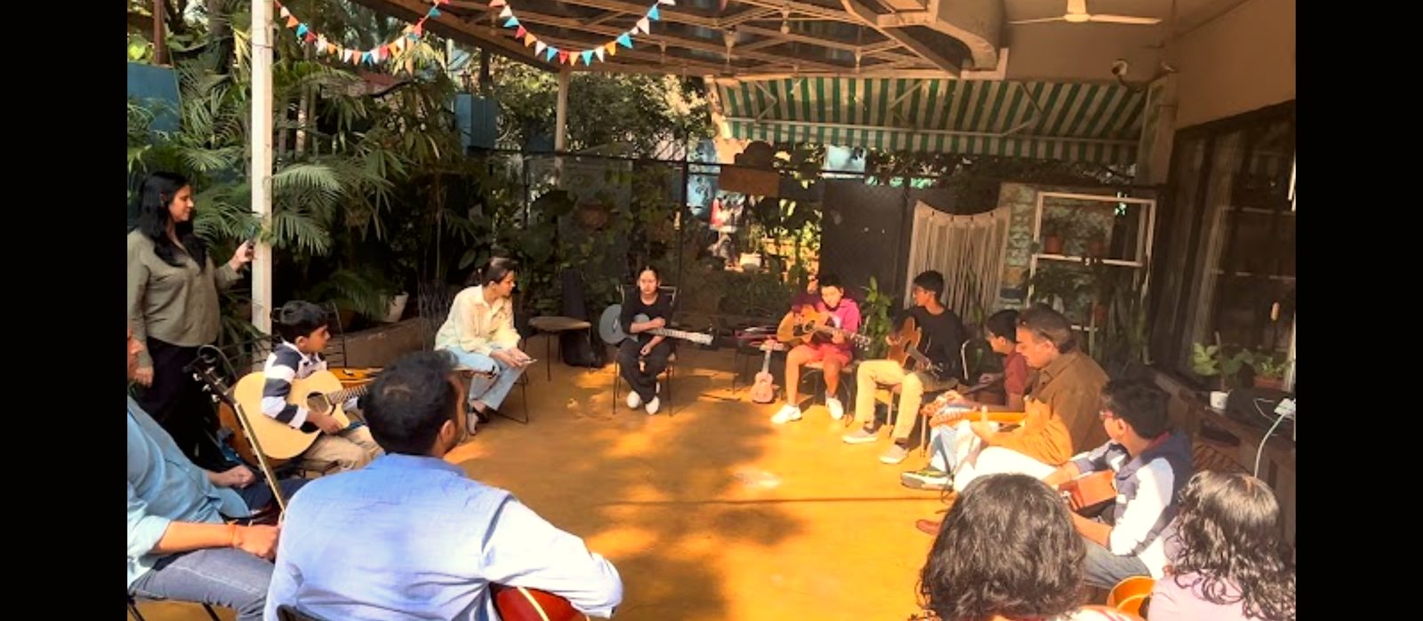 Children and teenagers playing guitars together in a circle outdoors at a Long Play jam session in Pune